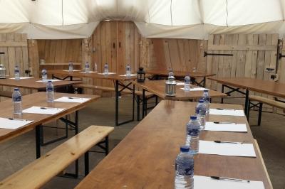 Groupe de personnes rassemblées en extérieur près de tentes et d'une table avec des verres, dans un cadre naturel.
