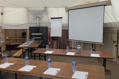 Groupe de personnes rassemblées en extérieur près de tentes et d'une table avec des verres, dans un cadre naturel.