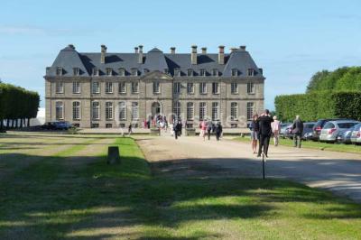Chambre lumineuse avec lit à baldaquin, armoire à miroir, chaise en bois et rideaux rouges encadrant une fenêtre ouverte.