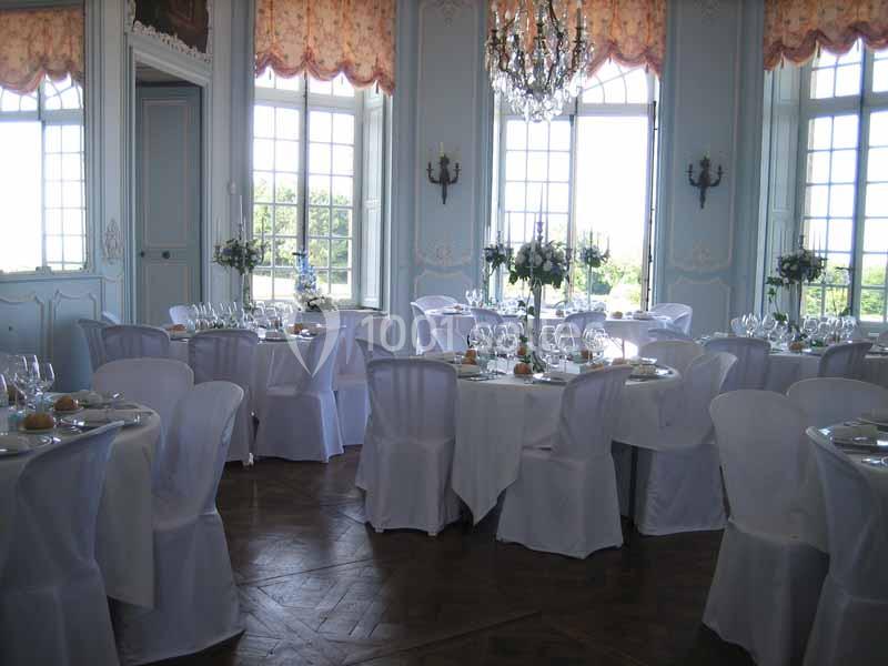 Salle de réception élégante avec tables rondes dressées, nappes blanches et grandes fenêtres laissant entrer la lumière.
