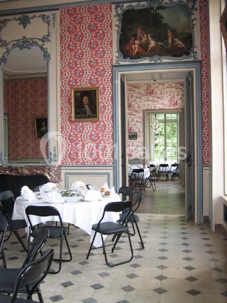 Salle à manger élégante avec tables dressées, chaises noires pliantes, murs ornés de motifs rouges et cadres anciens.