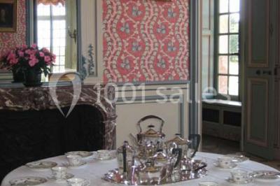 Chambre lumineuse avec lit à baldaquin, armoire à miroir, chaise en bois et rideaux rouges encadrant une fenêtre ouverte.