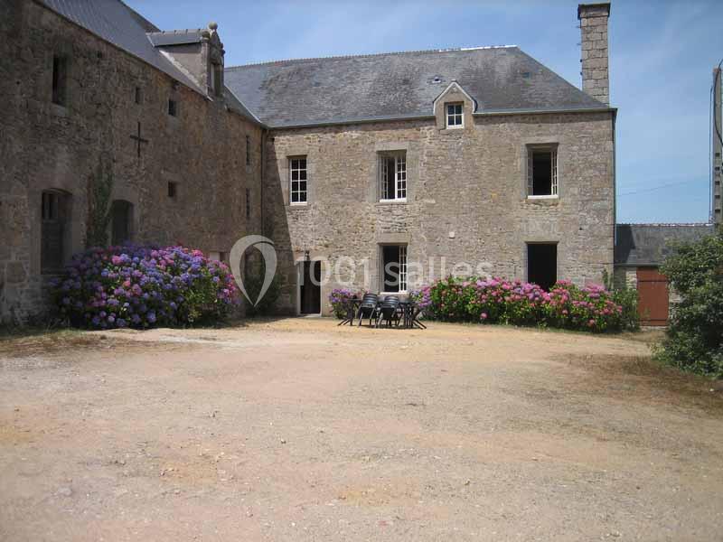Cour d'une maison en pierre avec des hortensias en fleurs et une table entourée de chaises au centre.