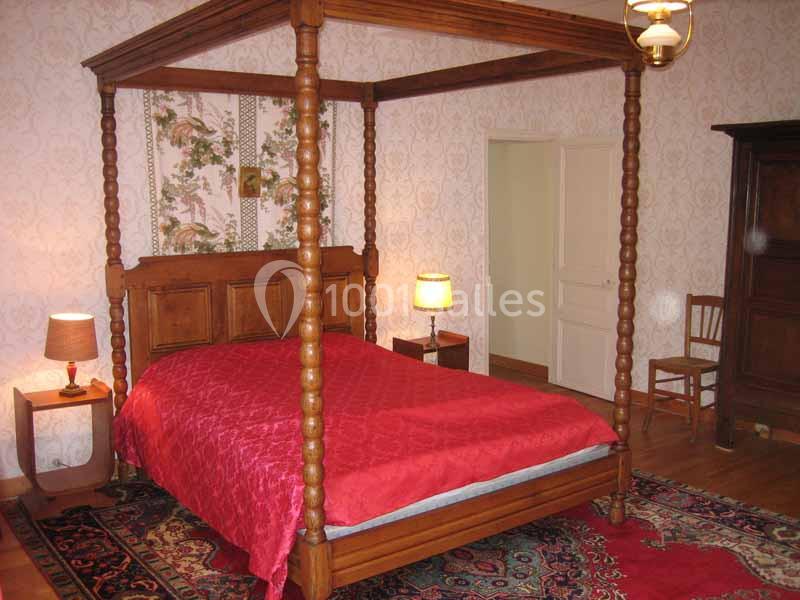 Lit à baldaquin en bois avec couvre-lit rouge, dans une chambre décorée de papier peint floral et meubles anciens.