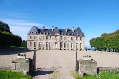 Vue d'un village avec des maisons entourées de verdure, un chemin en premier plan et la mer à l'horizon sous un ciel bleu.