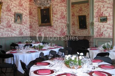 Vue d'un village avec des maisons entourées de verdure, un chemin en premier plan et la mer à l'horizon sous un ciel bleu.