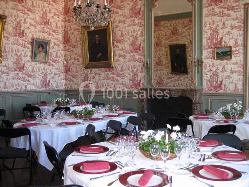 Salle élégante avec tables rondes dressées, nappes blanches, serviettes rouges, décor mural classique et cheminée en arrière…
