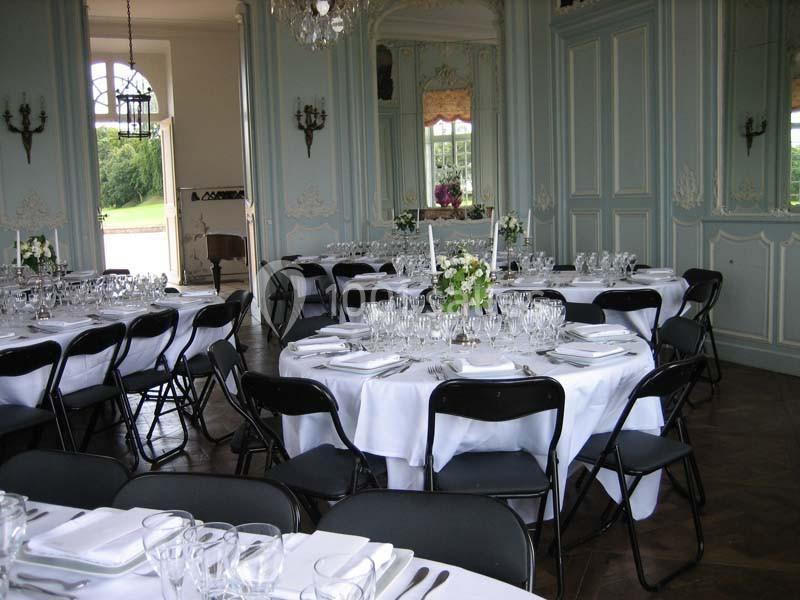 Salle élégante avec tables rondes dressées de nappes blanches, couverts et verres, entourées de chaises noires pliantes.