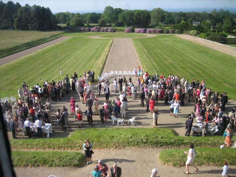 Groupe de personnes rassemblées dans un jardin avec des allées et une pelouse, lors d'un événement en plein air.