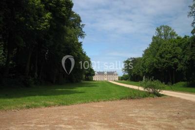 Vue d'un village avec des maisons entourées de verdure, un chemin en premier plan et la mer à l'horizon sous un ciel bleu.