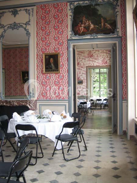 Salle à manger élégante avec murs ornés de motifs rouges, tables dressées et chaises pliantes noires.