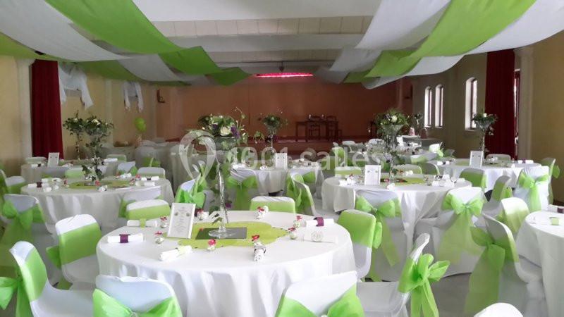 Salle de réception décorée avec des nappes blanches, des rubans verts et des centres de table fleuris.