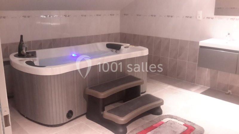 Baignoire spa avec marches antidérapantes dans une salle de bain carrelée sous un plafond mansardé.