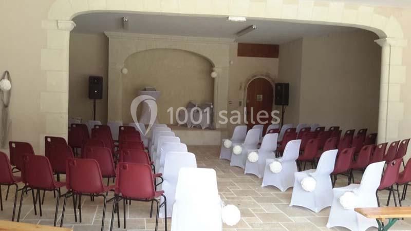 Salle aménagée pour une cérémonie avec des chaises blanches et rouges disposées face à une petite estrade.