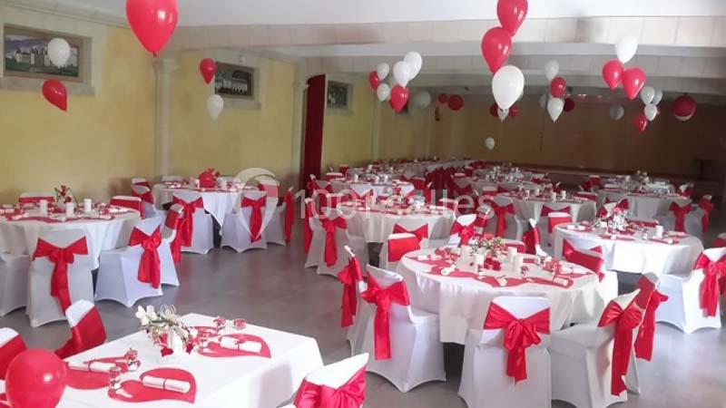 Salle de réception décorée avec des nappes blanches, des nœuds rouges sur les chaises et des ballons rouges et blancs.