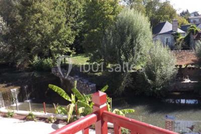 Miniature Location salle Onzain (Loir-et-Cher) - Le Manoir du Moulin #24 Vue depuis une terrasse rouge sur un petit cours d'eau bordé d'arbres, avec des maisons en arrière-plan.