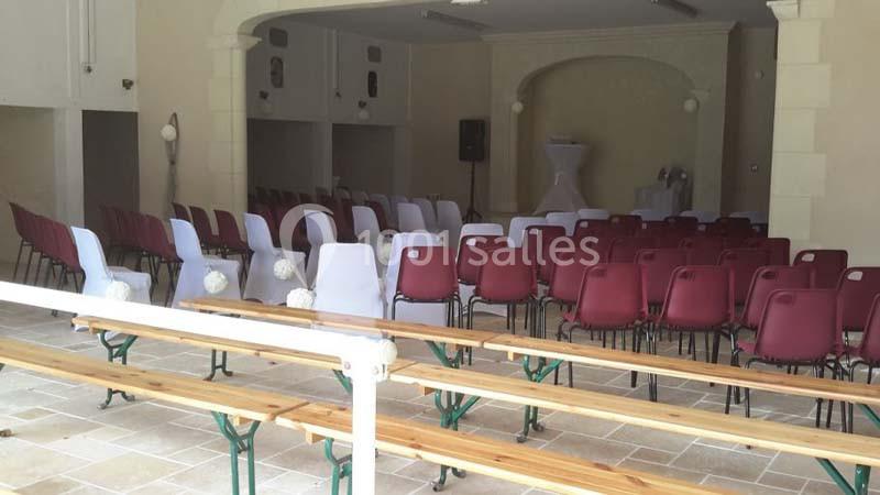 Salle aménagée avec des rangées de chaises blanches et rouges, et des bancs en bois, prête pour un événement.