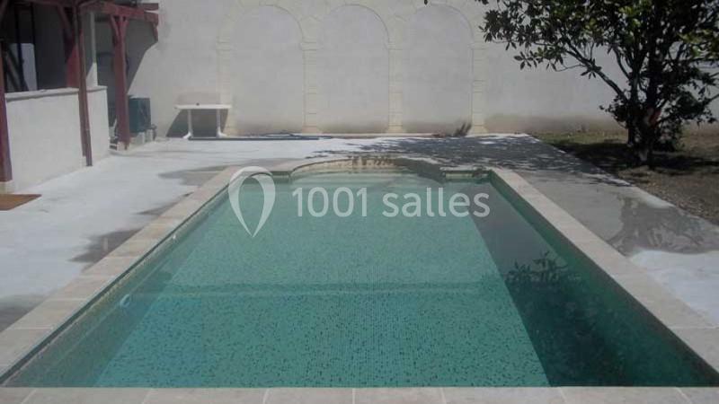 Piscine rectangulaire avec margelles claires, entourée d'une terrasse en béton et d'un mur beige avec arches.
