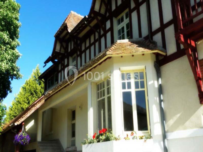 Façade d'une maison à colombages avec des fenêtres blanches, un toit en tuiles et des fleurs en premier plan.