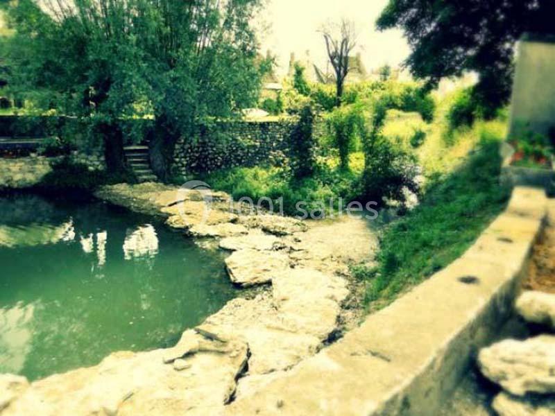 Petit cours d'eau bordé de pierres et de végétation, avec un mur en pierre et des arbres en arrière-plan.