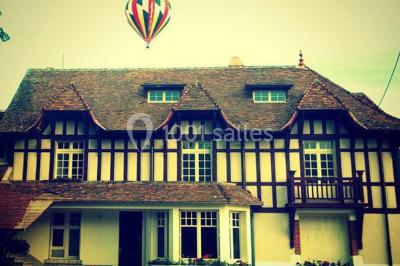 Miniature Location salle Onzain (Loir-et-Cher) - Le Manoir du Moulin #2 Vue depuis une terrasse rouge sur un petit cours d'eau bordé d'arbres, avec des maisons en arrière-plan.