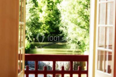 Miniature Location salle Onzain (Loir-et-Cher) - Le Manoir du Moulin #8 Vue depuis une terrasse rouge sur un petit cours d'eau bordé d'arbres, avec des maisons en arrière-plan.