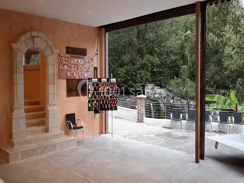 Vue d'un espace intérieur ouvert sur un extérieur verdoyant, avec un présentoir d'objets et un escalier en pierre.