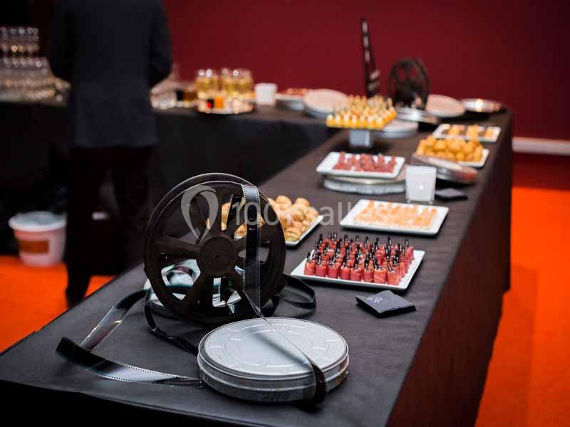 Bobines de film posées sur une table de buffet garnie de verrines et amuse-bouches dans une salle au sol orange.