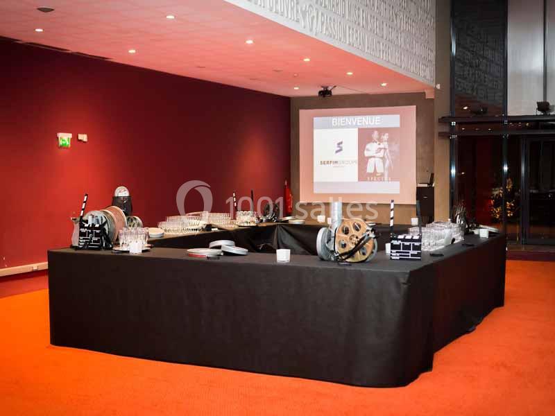 Table dressée avec des accessoires de cinéma, verres et projecteur affichant un écran de bienvenue dans une salle rouge.