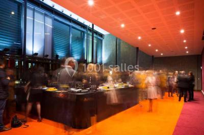 Vue intérieure d'un espace de loisirs avec sièges, tables, escalier central et décorations colorées sous un plafond haut.