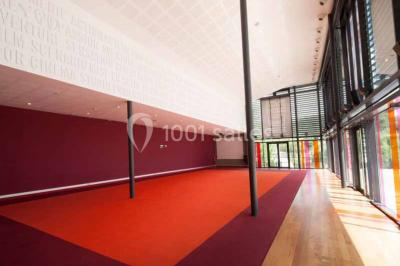 Vue intérieure d'un espace de loisirs avec sièges, tables, escalier central et décorations colorées sous un plafond haut.