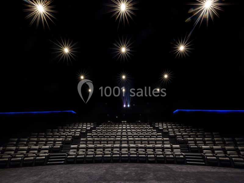 Salle de cinéma vide avec rangées de sièges alignés et éclairage tamisé provenant de spots lumineux au plafond.