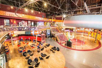 Vue intérieure d'un espace de loisirs avec sièges, tables, escalier central et décorations colorées sous un plafond haut.