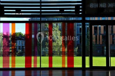 Vue intérieure d'un espace de loisirs avec sièges, tables, escalier central et décorations colorées sous un plafond haut.