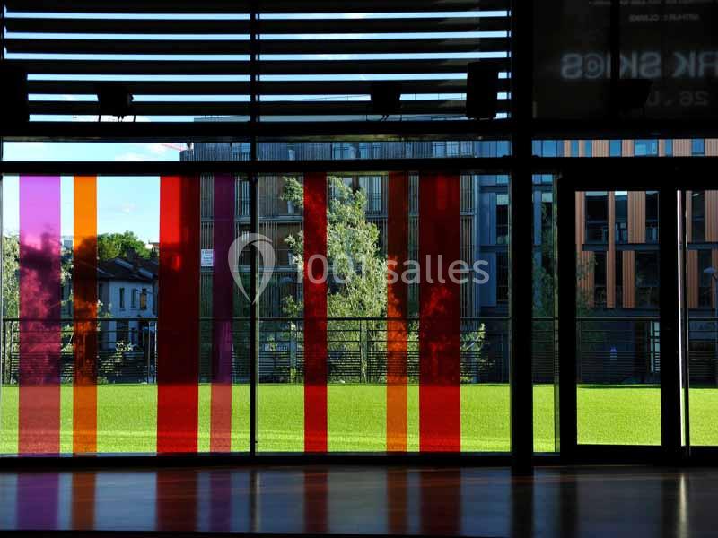 Baies vitrées colorées donnant sur un espace vert avec des bâtiments en arrière-plan.