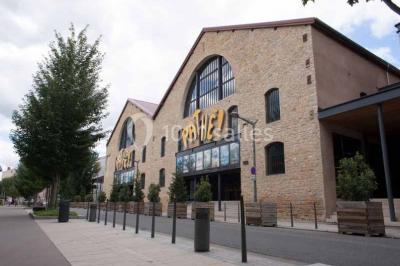 Vue intérieure d'un espace de loisirs avec sièges, tables, escalier central et décorations colorées sous un plafond haut.