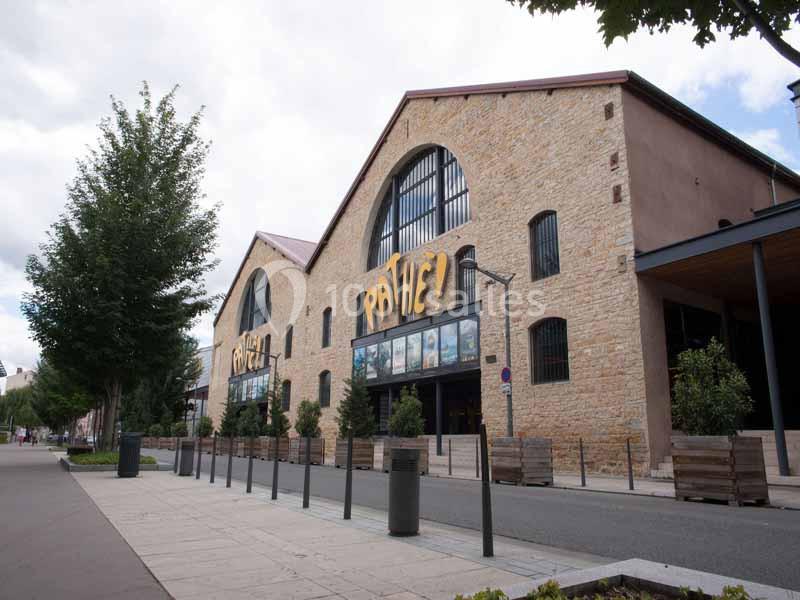 Façade d'un bâtiment en pierre avec des enseignes lumineuses, entouré d'arbres et d'une rue piétonne.
