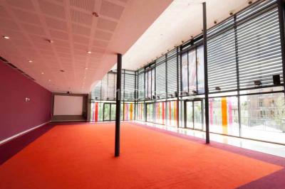 Vue intérieure d'un espace de loisirs avec sièges, tables, escalier central et décorations colorées sous un plafond haut.