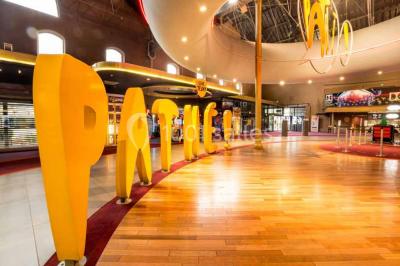 Vue intérieure d'un espace de loisirs avec sièges, tables, escalier central et décorations colorées sous un plafond haut.