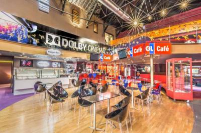 Vue intérieure d'un espace de loisirs avec sièges, tables, escalier central et décorations colorées sous un plafond haut.