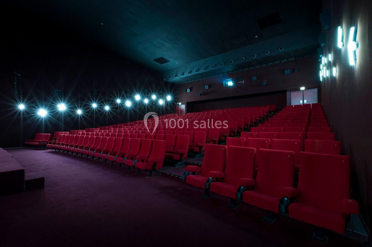 Salle de cinéma vide avec des rangées de fauteuils rouges et un éclairage tamisé sur les murs.