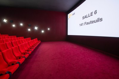 Salle de cinéma avec des sièges rouges, un écran géant affichant ’Salle 14, 241 fauteuils’ et un éclairage tamisé.