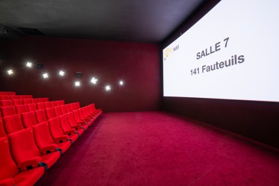 Salle de cinéma avec des sièges rouges, un écran géant affichant ’Salle 14, 241 fauteuils’ et un éclairage tamisé.