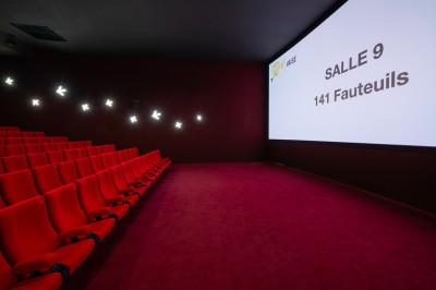 Salle de cinéma avec des sièges rouges, un écran géant affichant ’Salle 14, 241 fauteuils’ et un éclairage tamisé.