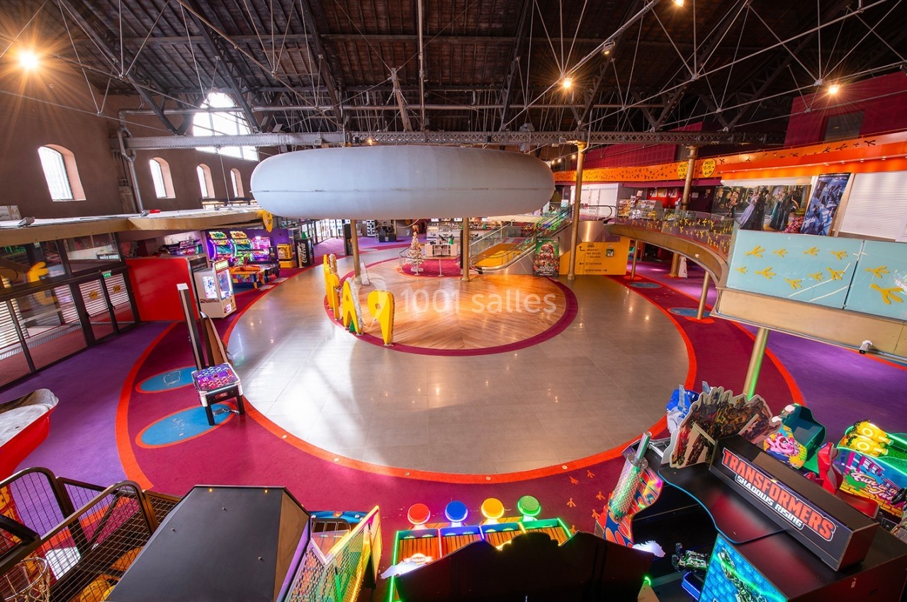 Vue intérieure d'une aire de jeux couverte avec des arcades, un espace central circulaire et des structures colorées.