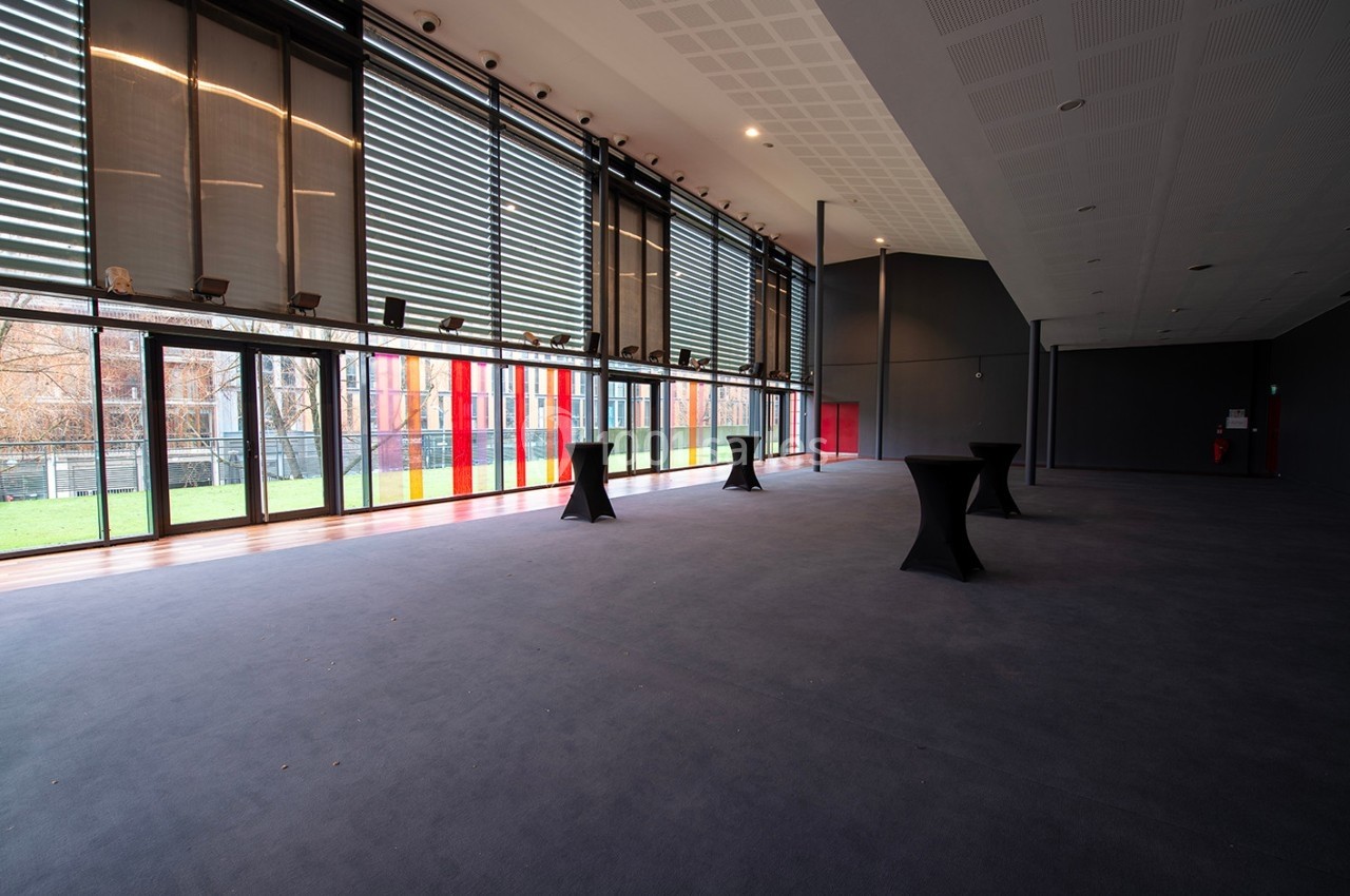 Salle spacieuse avec de grandes baies vitrées, des tables hautes noires et un sol recouvert de moquette sombre.