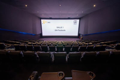 Salle de cinéma avec des sièges rouges, un écran géant affichant ’Salle 14, 241 fauteuils’ et un éclairage tamisé.