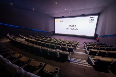 Salle de cinéma avec des sièges rouges, un écran géant affichant ’Salle 14, 241 fauteuils’ et un éclairage tamisé.