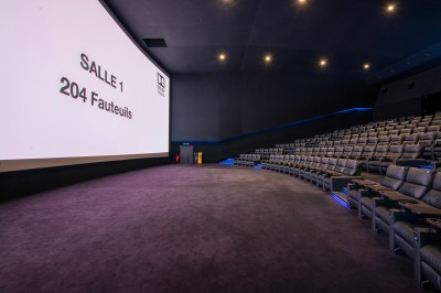 Salle de cinéma avec des sièges rouges, un écran géant affichant ’Salle 14, 241 fauteuils’ et un éclairage tamisé.