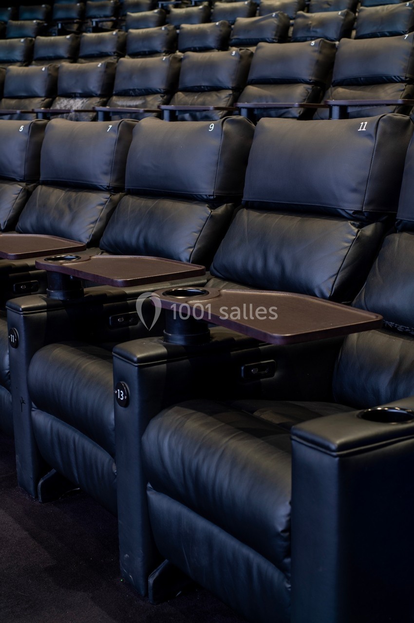 Fauteuils de cinéma en cuir noir avec tablettes et porte-gobelets intégrés, alignés dans une salle vide.